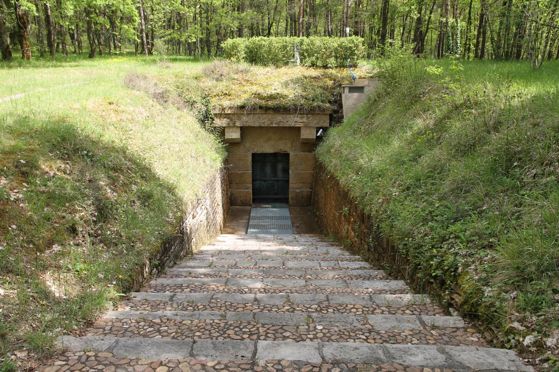 L’entrée de la grotte de Lascaux : une porte de bronze au fond d’un escalier de pierre, scellée dans un talus herbeux
