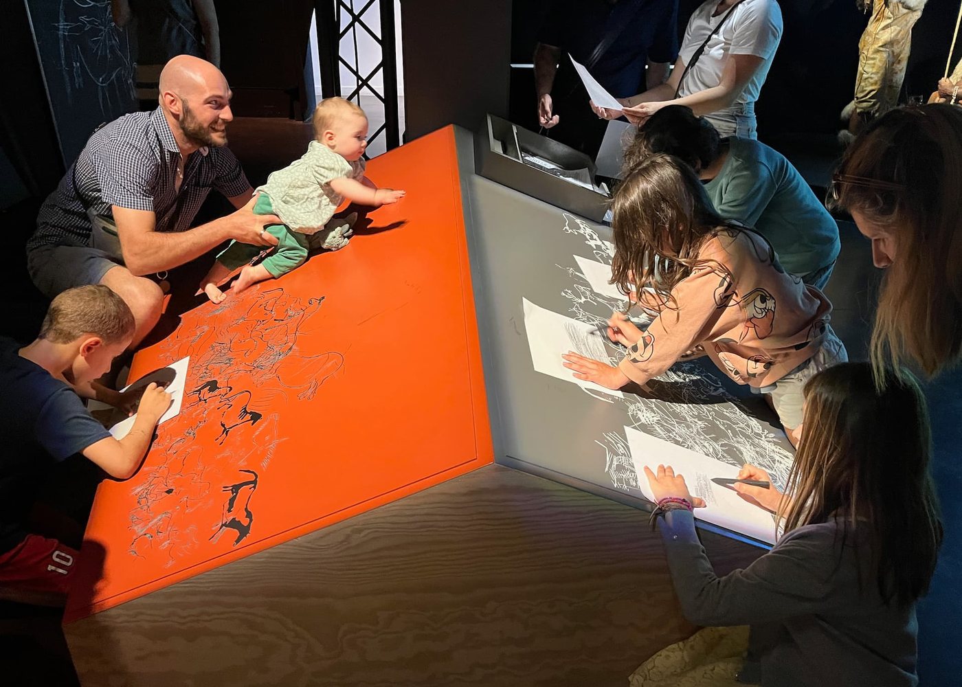 Families around a sloping workshop table, adults and children drawing side by side