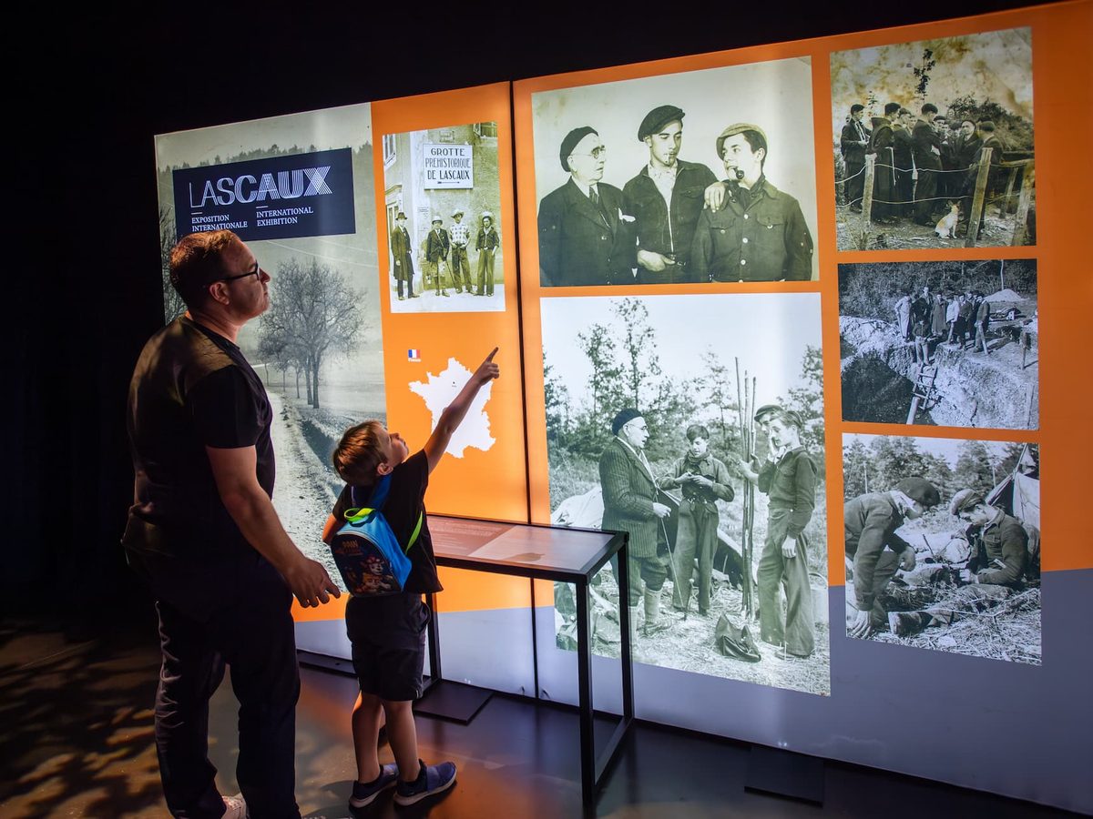 A father and child in front of the “An extraordinary discovery” module, showing archive photographs of the cave’s discoverers