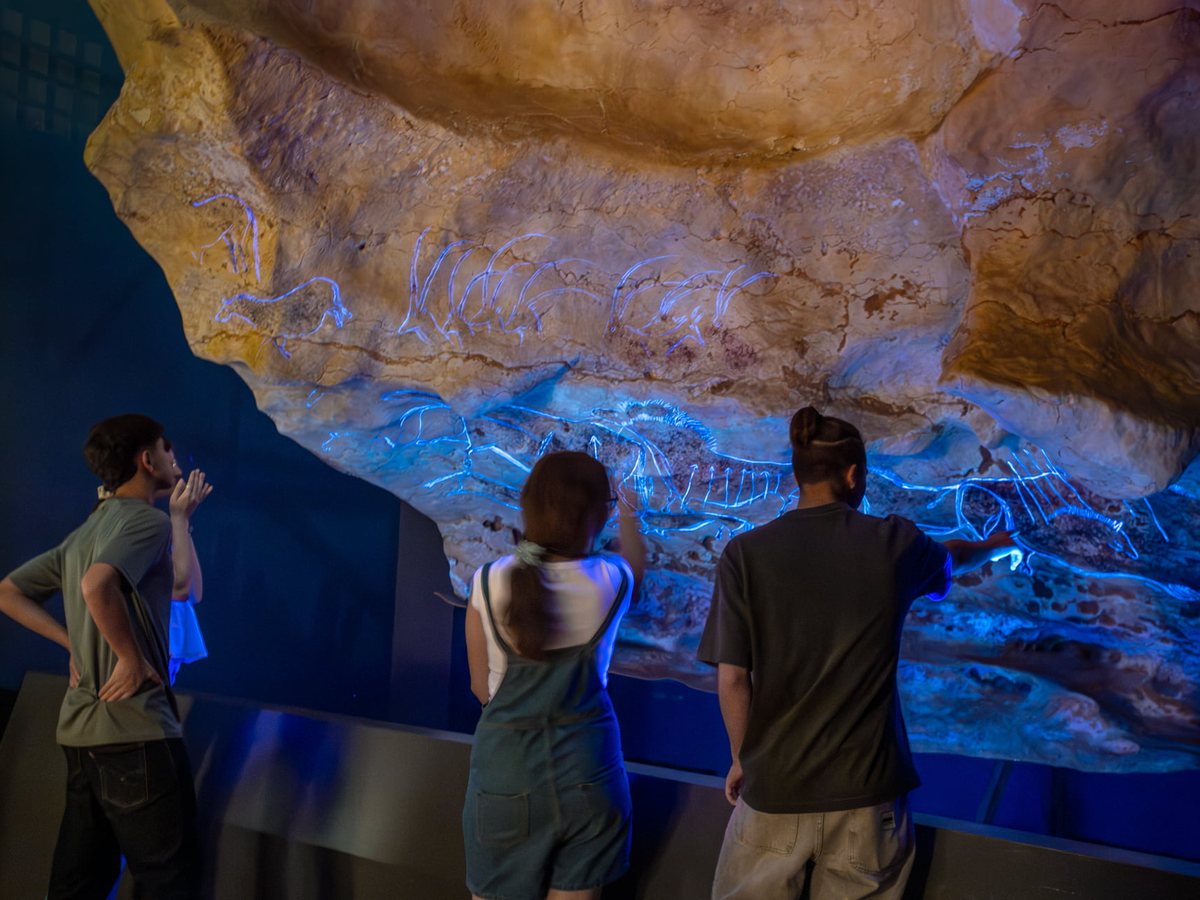 Three visitors facing the Panel of the Imprint, where blue lighting reveals the engravings