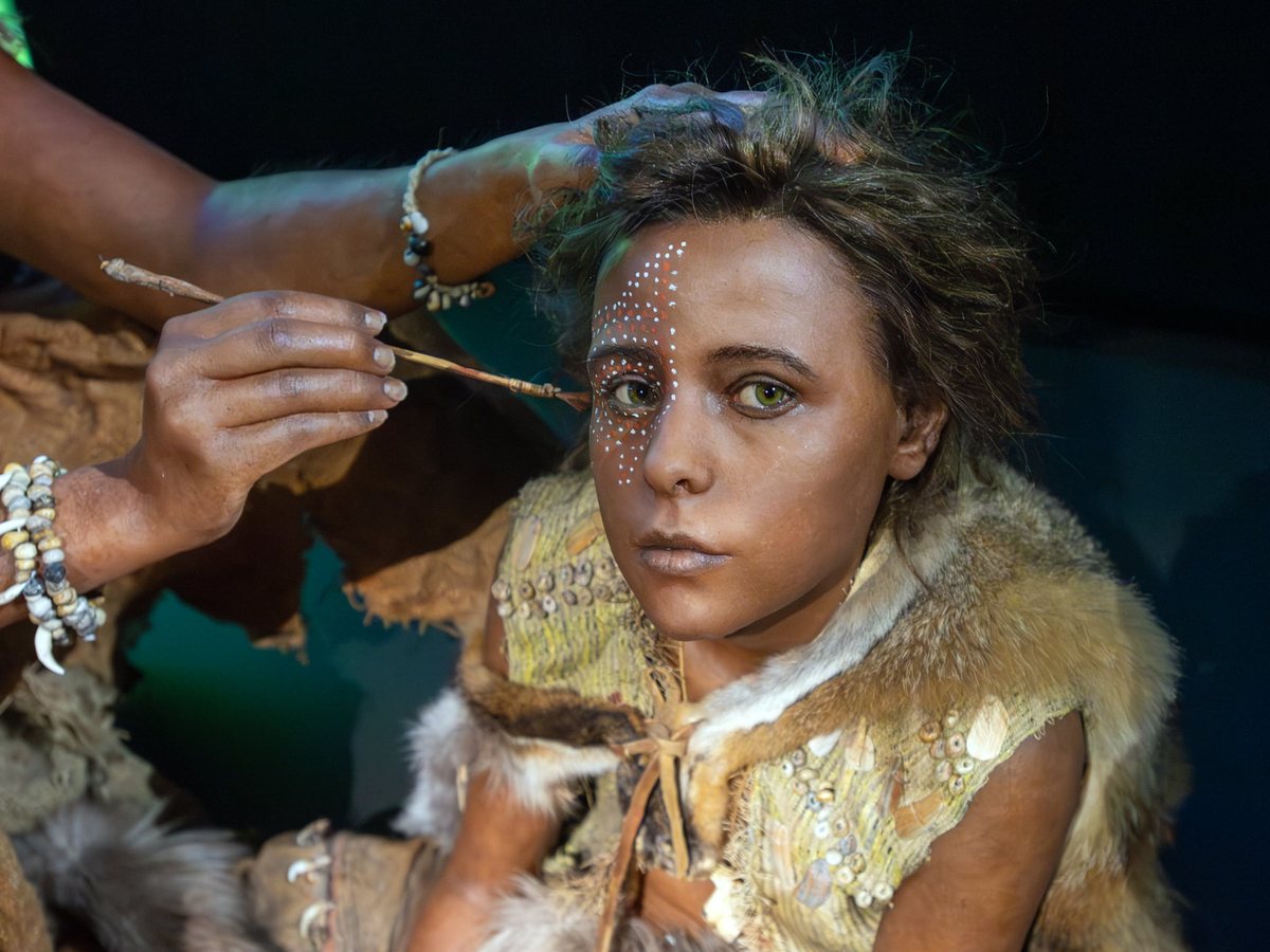 Une main applique un pigment blanc sur le visage d’une reconstitution d’adolescente