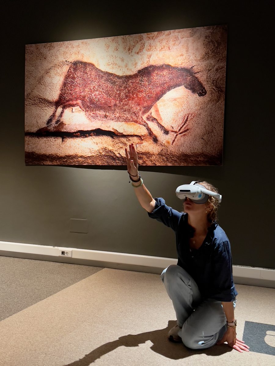 A visitor wearing a headset raises her hand towards the horse on the wall